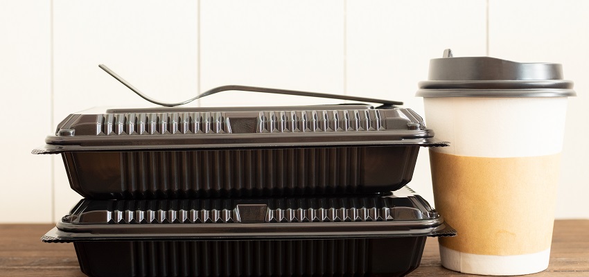 Closeup of two black to-go containers stacked on top of each other with a white to-go coffee cup next to them on a wood table