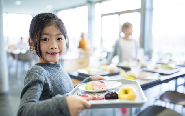 photo of a young female student carrying tray of lunch food in a cafeteria