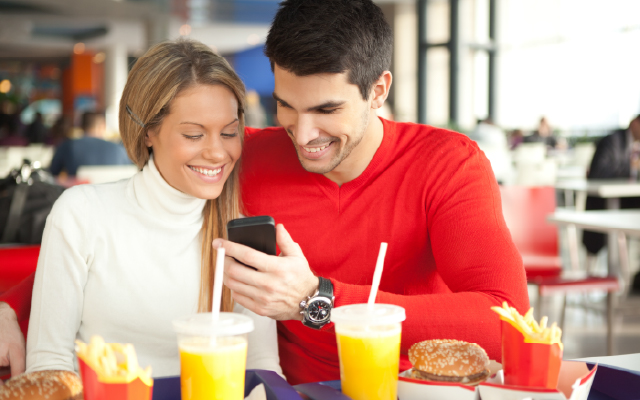 photo of a woman and man looking at a cell phone while having a fast-food meal