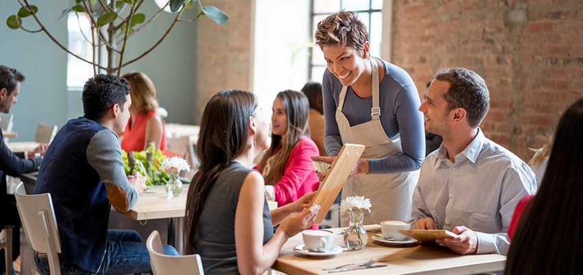 Friendly waitress serving couple at a restaurant taking orders and looking very happy